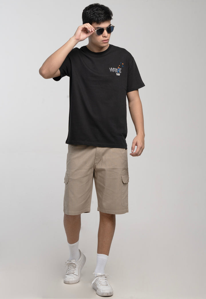 Person wearing a black t-shirt and beige shorts with sunglasses on a plain background