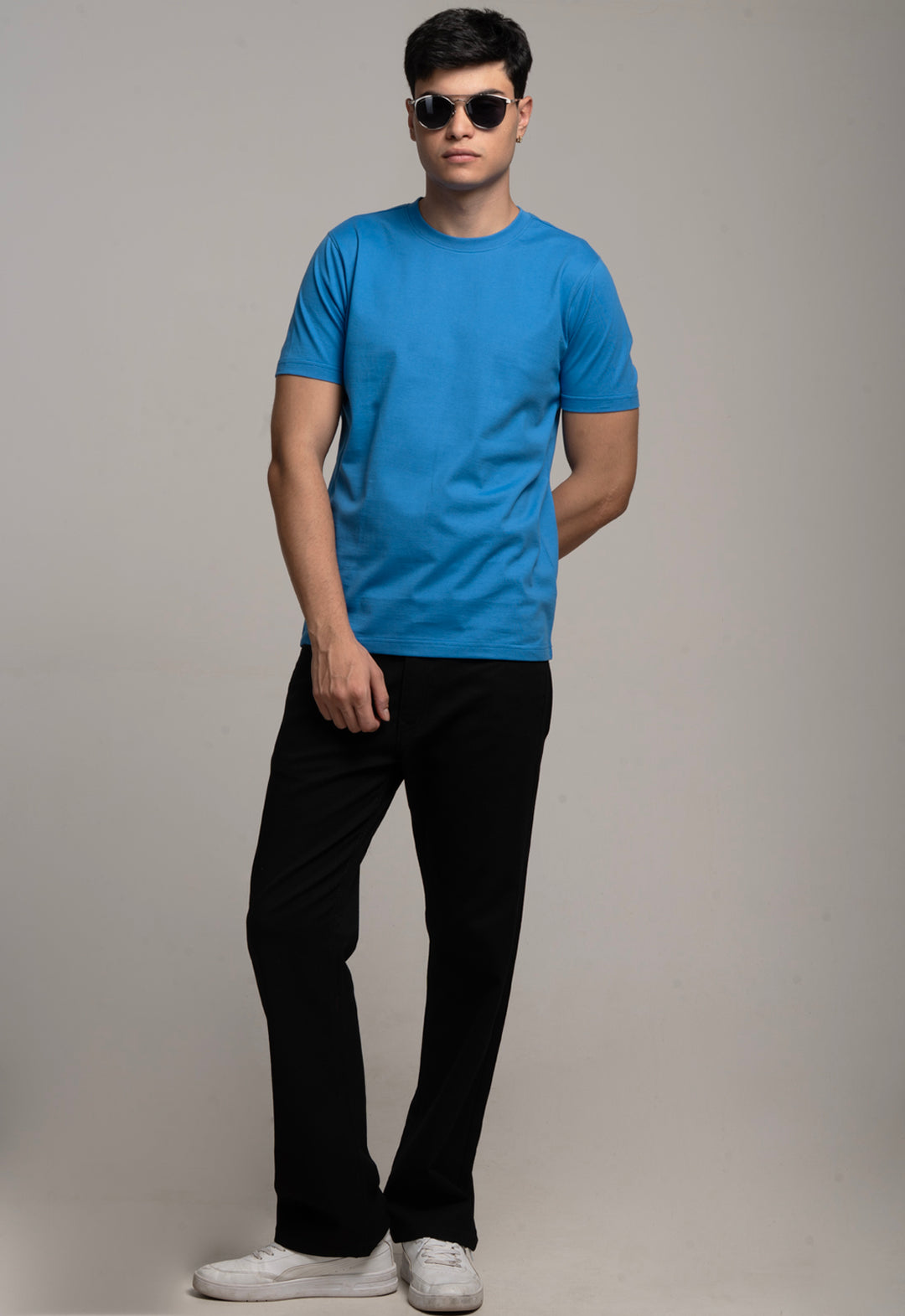 Man wearing a blue t-shirt, black pants, and sunglasses against a gray background
