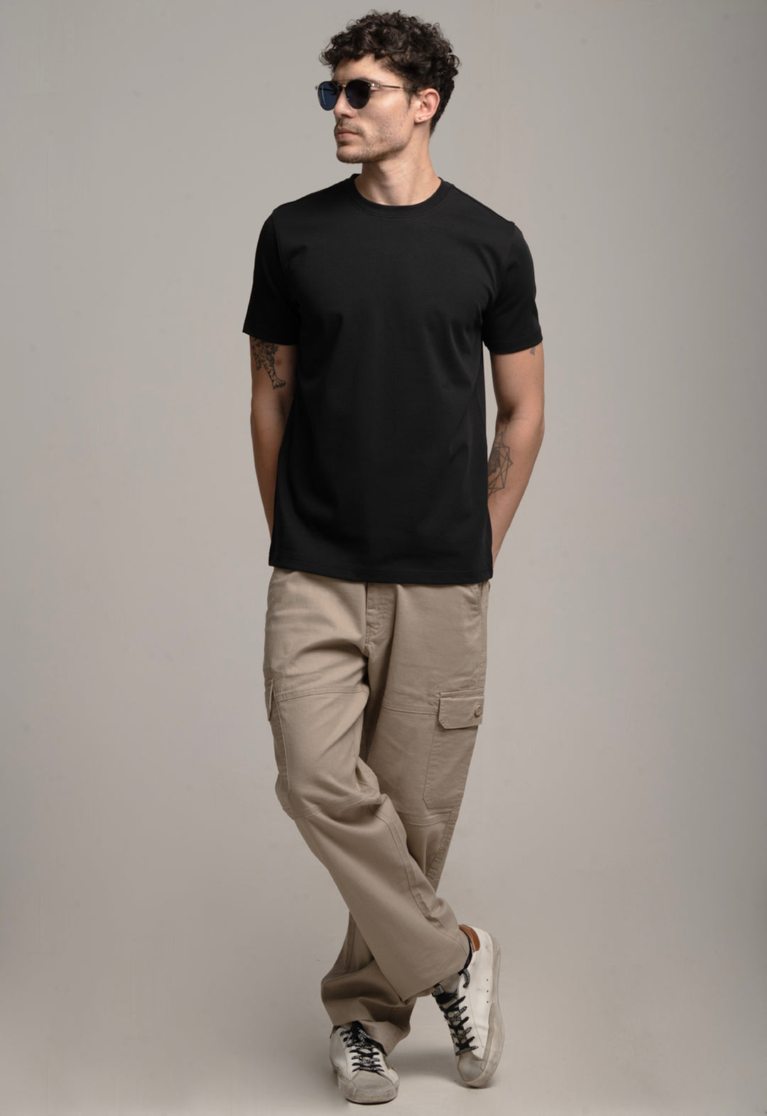 Man wearing a black t-shirt, beige pants, and sunglasses against a gray background