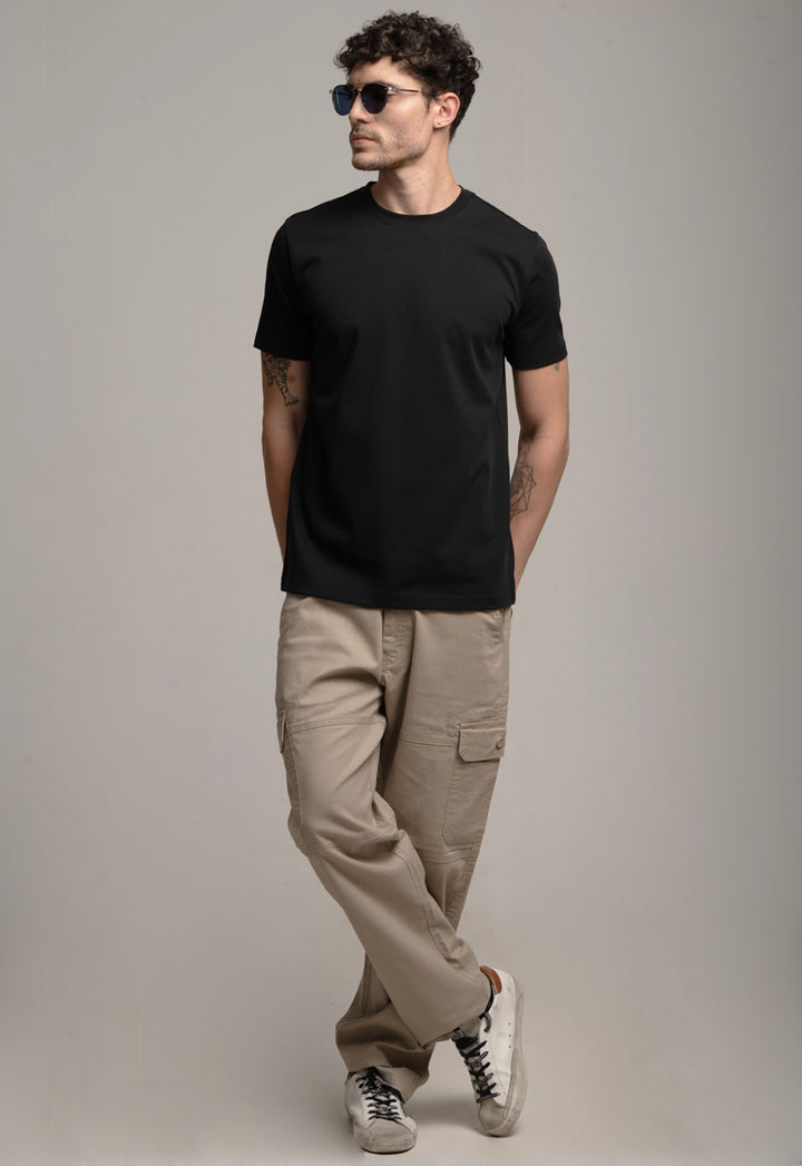 Man wearing a black t-shirt, beige pants, and sunglasses against a gray background