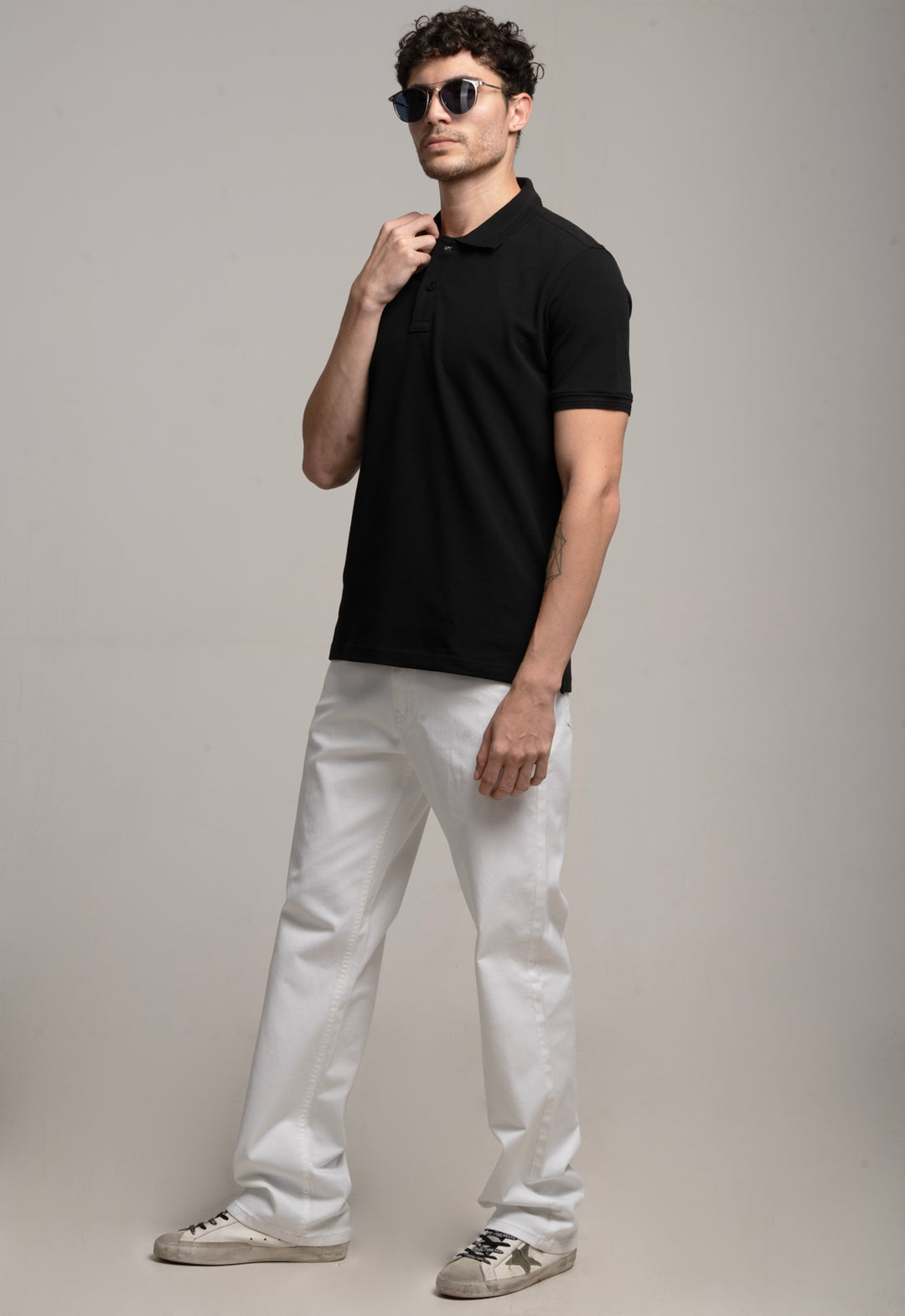 Man wearing a black polo shirt and white pants against a gray background