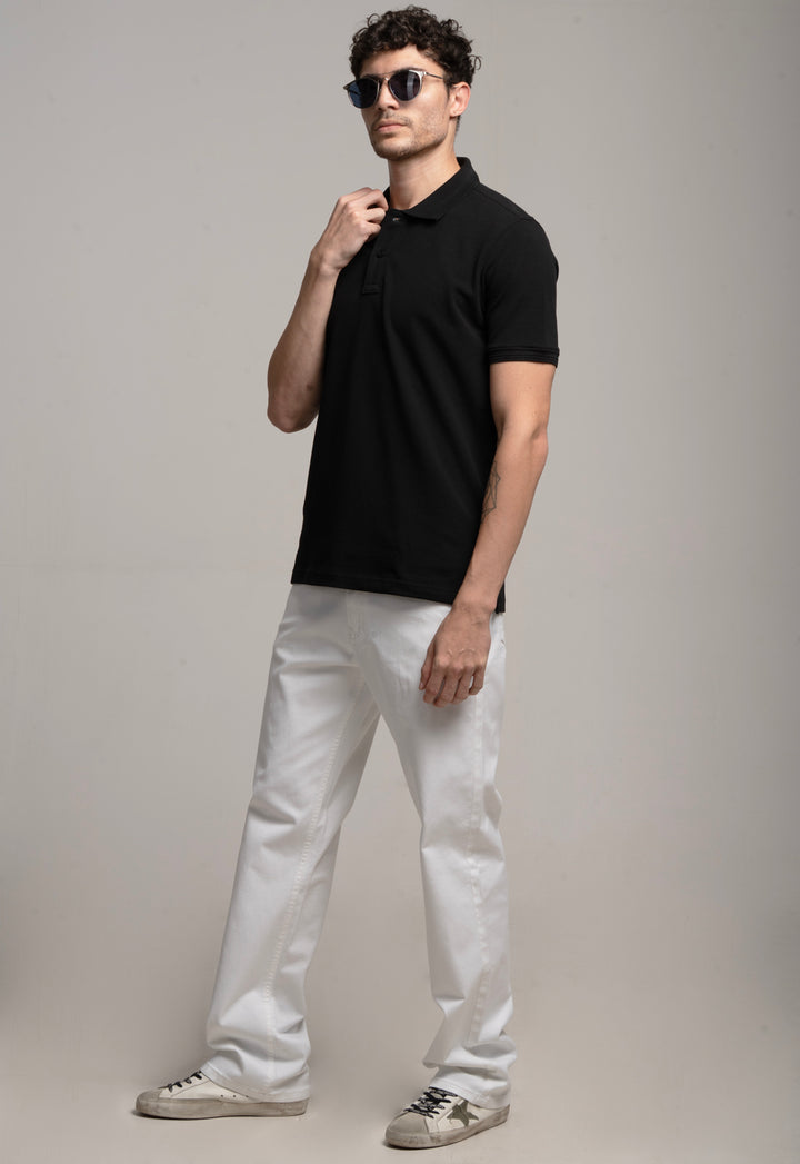 Man wearing a black polo shirt and white pants against a gray background