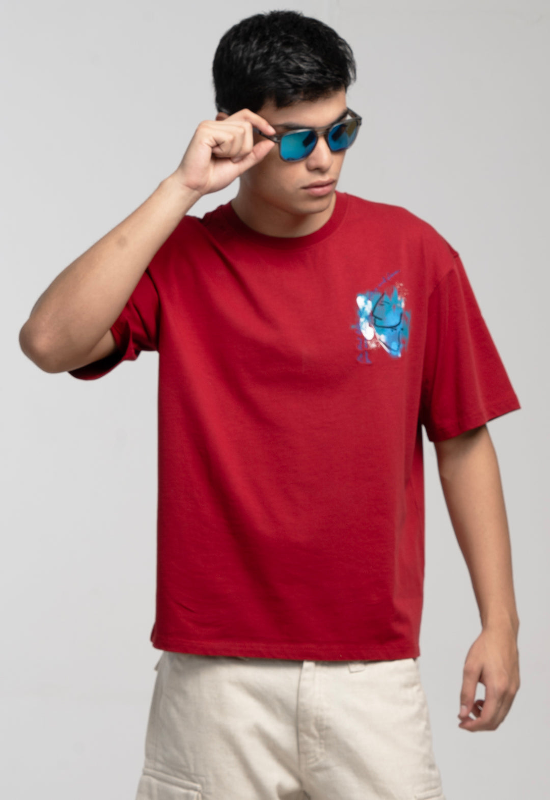 Person wearing a red t-shirt with a graphic design, holding sunglasses, on a plain background