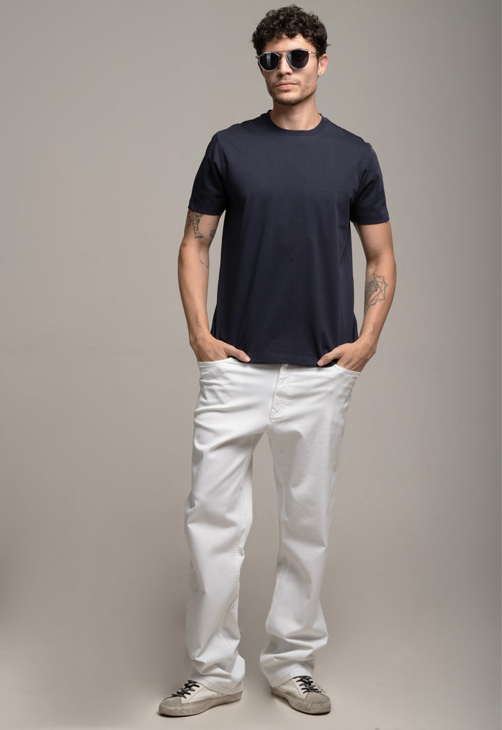 Man wearing a navy t-shirt and white pants against a gray background