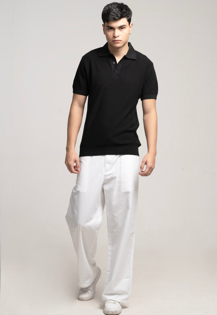 Man wearing a black polo shirt and white pants on a plain background