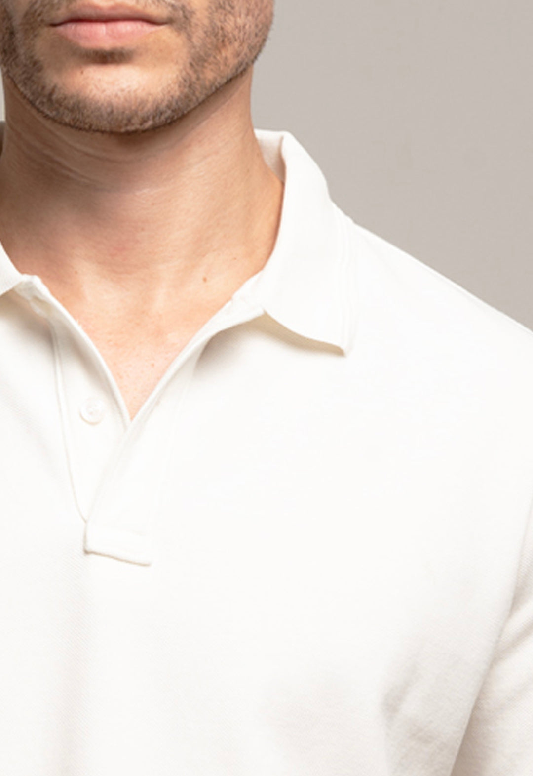 Close-up of a person wearing a white polo shirt against a neutral background