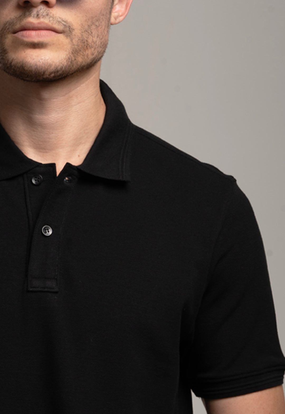 Man wearing a black polo shirt against a gray background