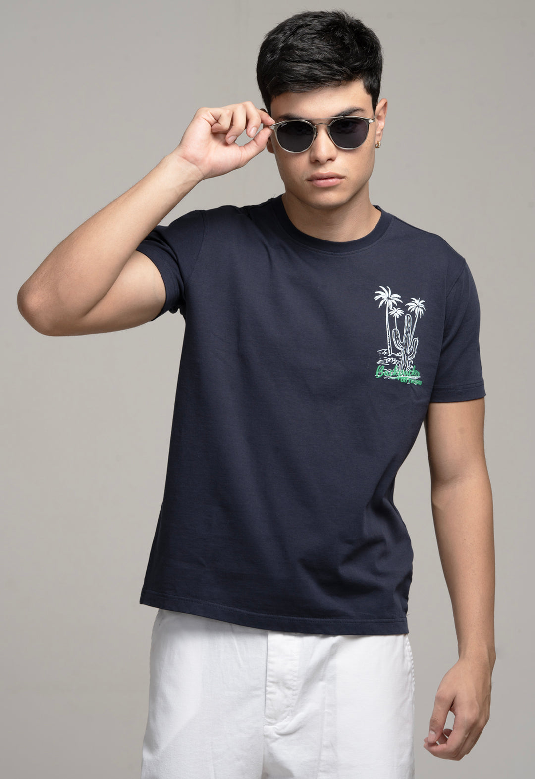 Man wearing a navy blue t-shirt with a palm tree design, holding sunglasses.