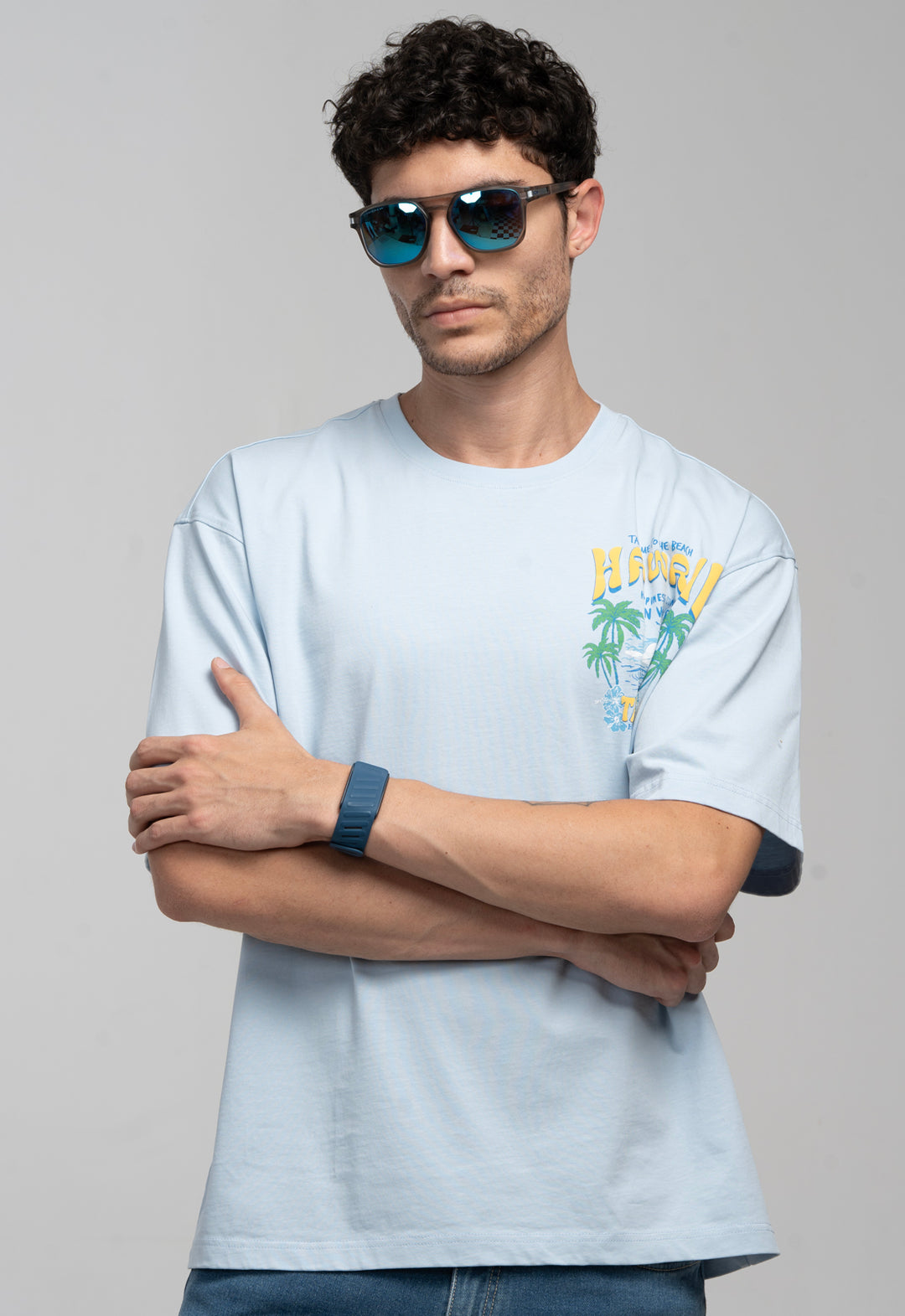 Man wearing a light blue t-shirt with a graphic design, sunglasses, and a watch on a gray background