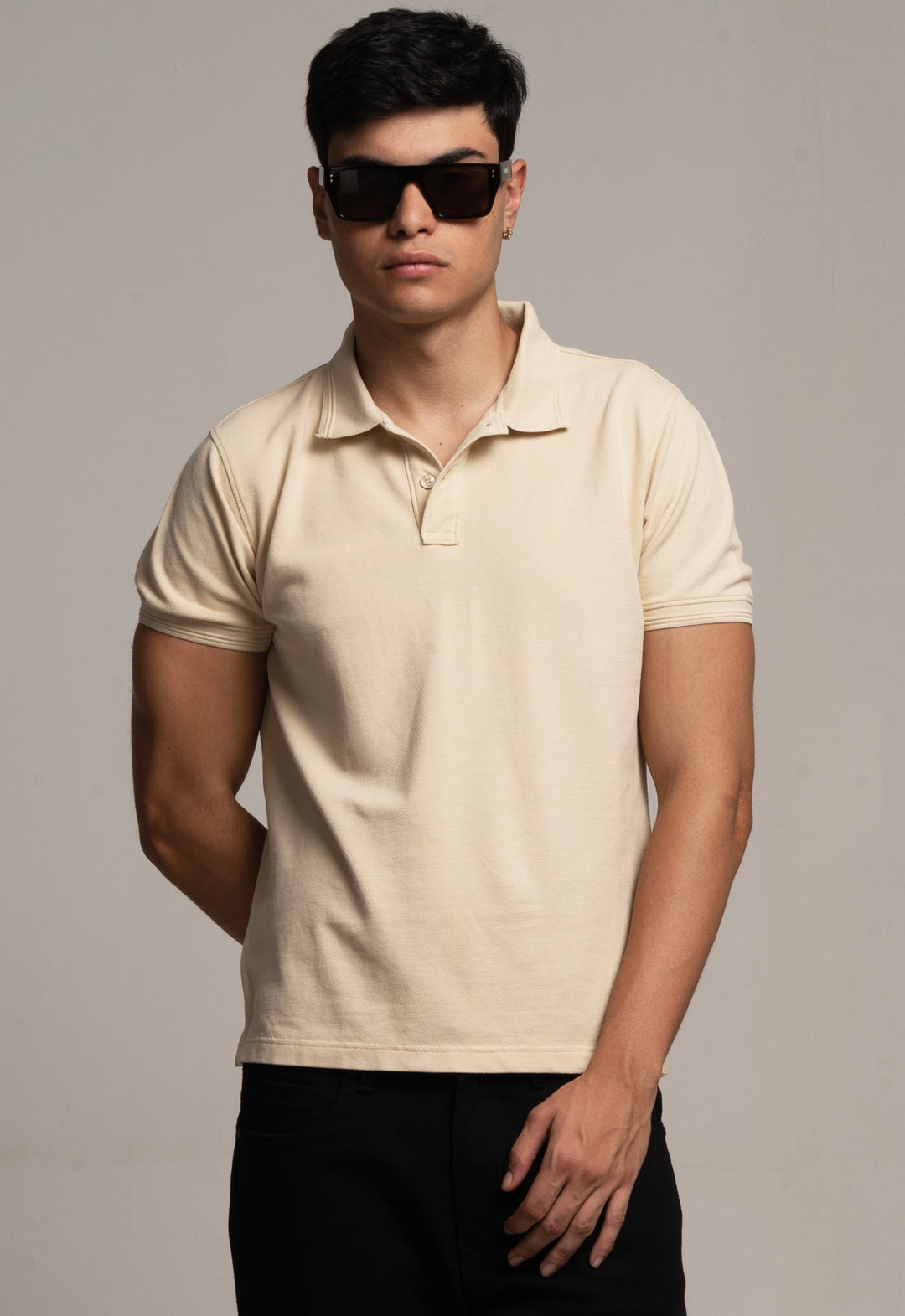 Man wearing a beige polo shirt and sunglasses against a plain background