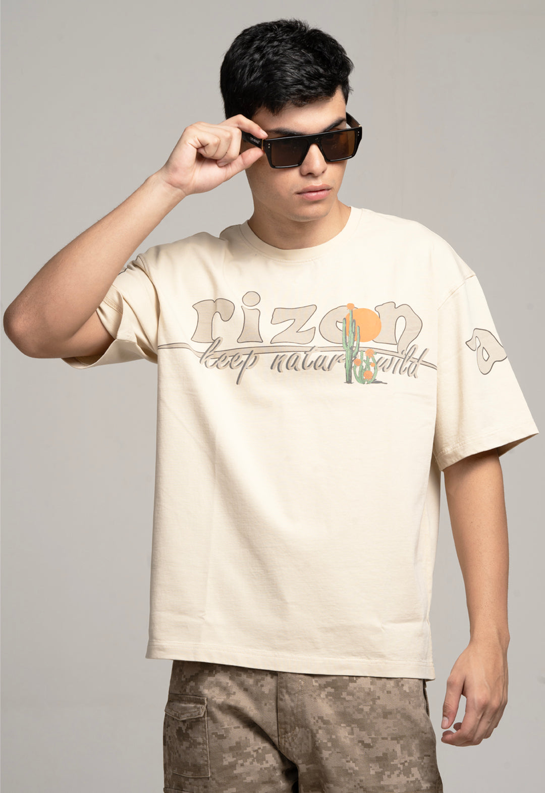 Person wearing a beige t-shirt with 'rizon' branding and sunglasses, against a plain background
