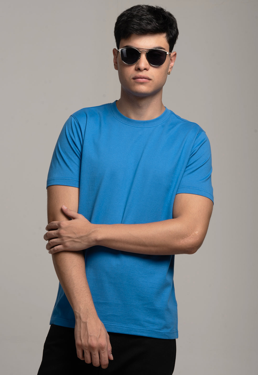 Man wearing a blue t-shirt and sunglasses against a gray background