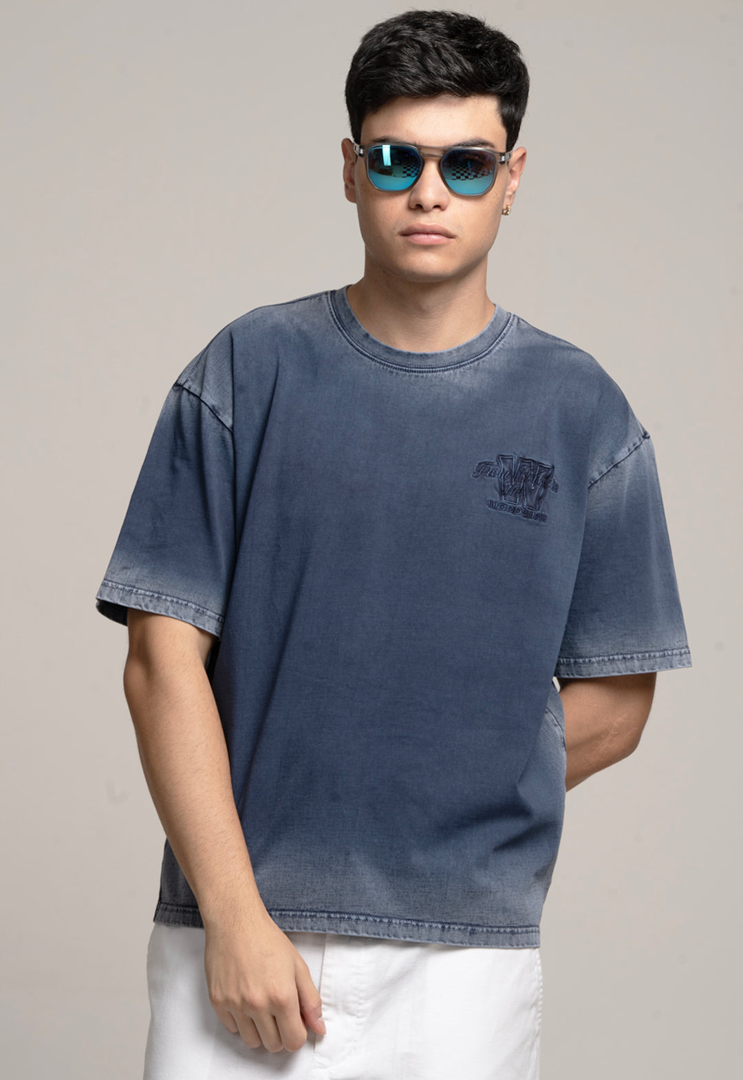 Man wearing a blue t-shirt and sunglasses against a plain background
