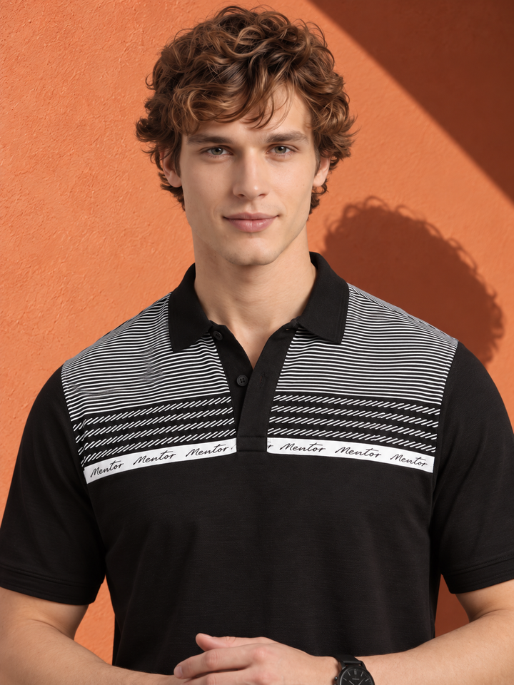 A man wearing a black short-sleeve polo shirt with a black and white striped yoke and a white band across the chest, posed against a textured orange wall.