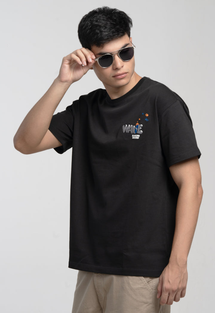 Person wearing a black t-shirt with a logo, holding sunglasses, on a plain background