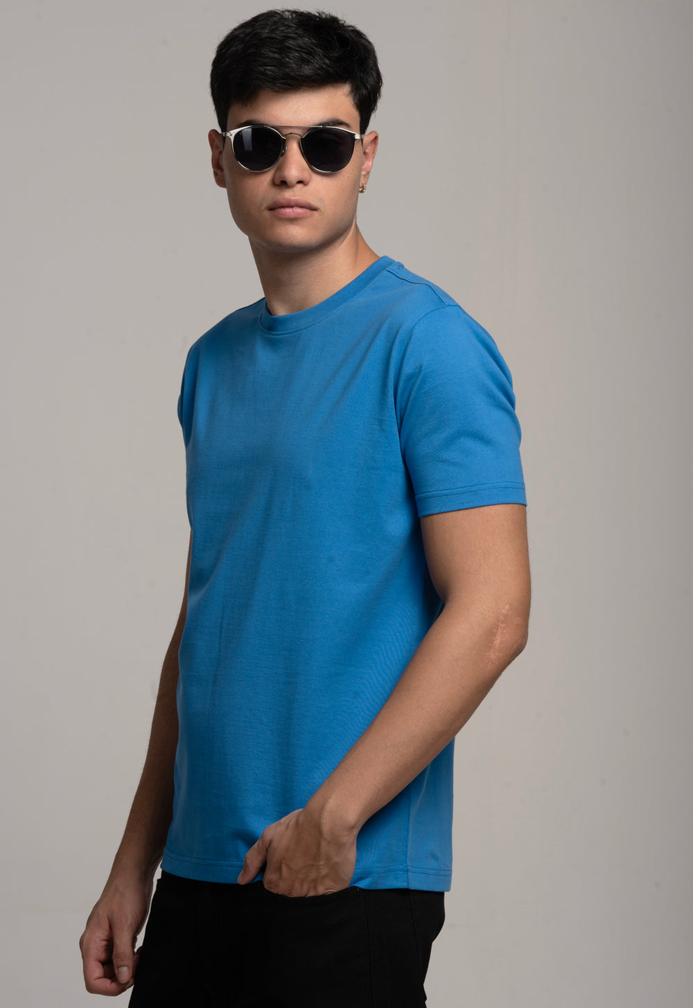 Man wearing a blue t-shirt and sunglasses against a gray background