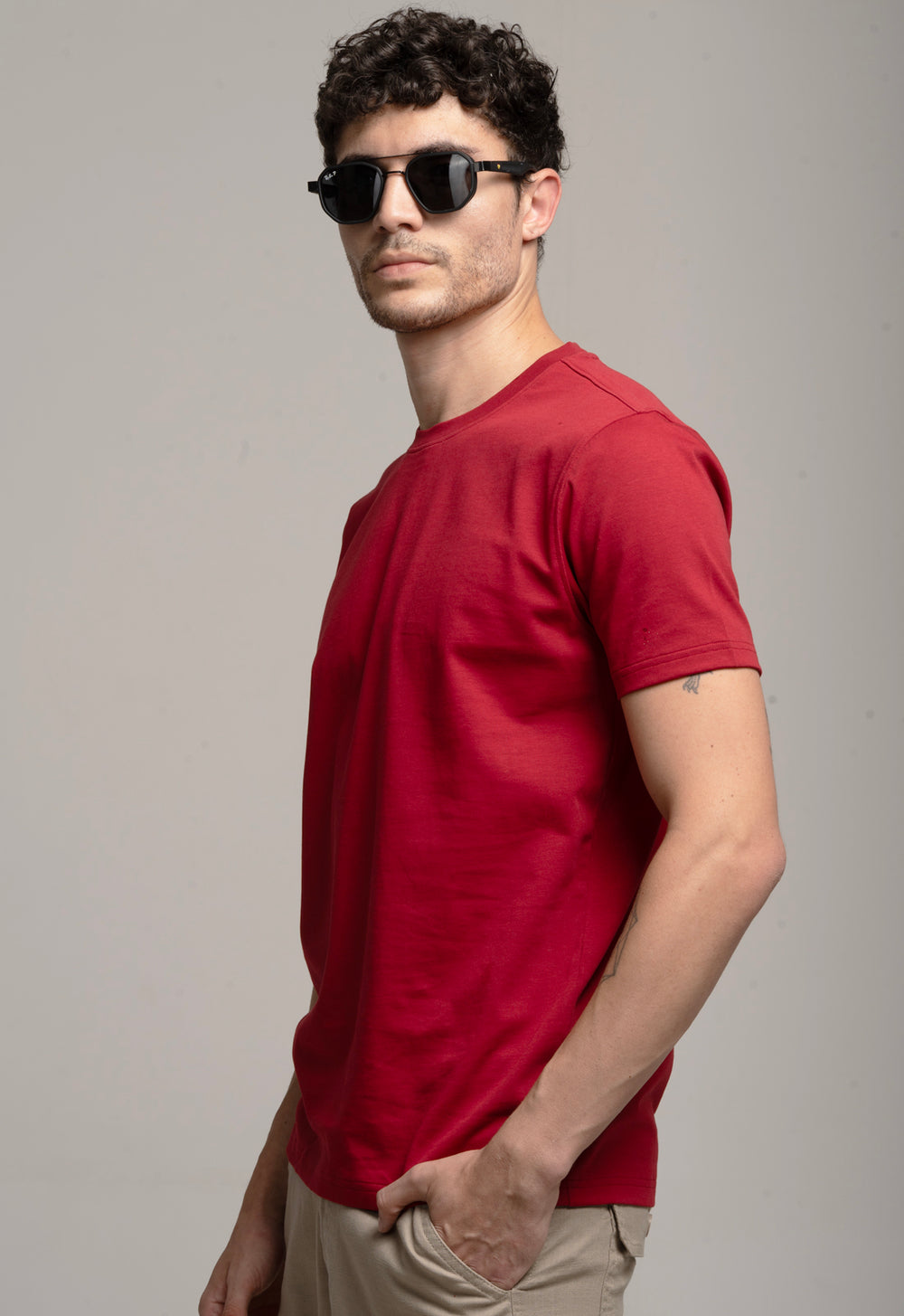 Man wearing a red t-shirt and sunglasses against a gray background
