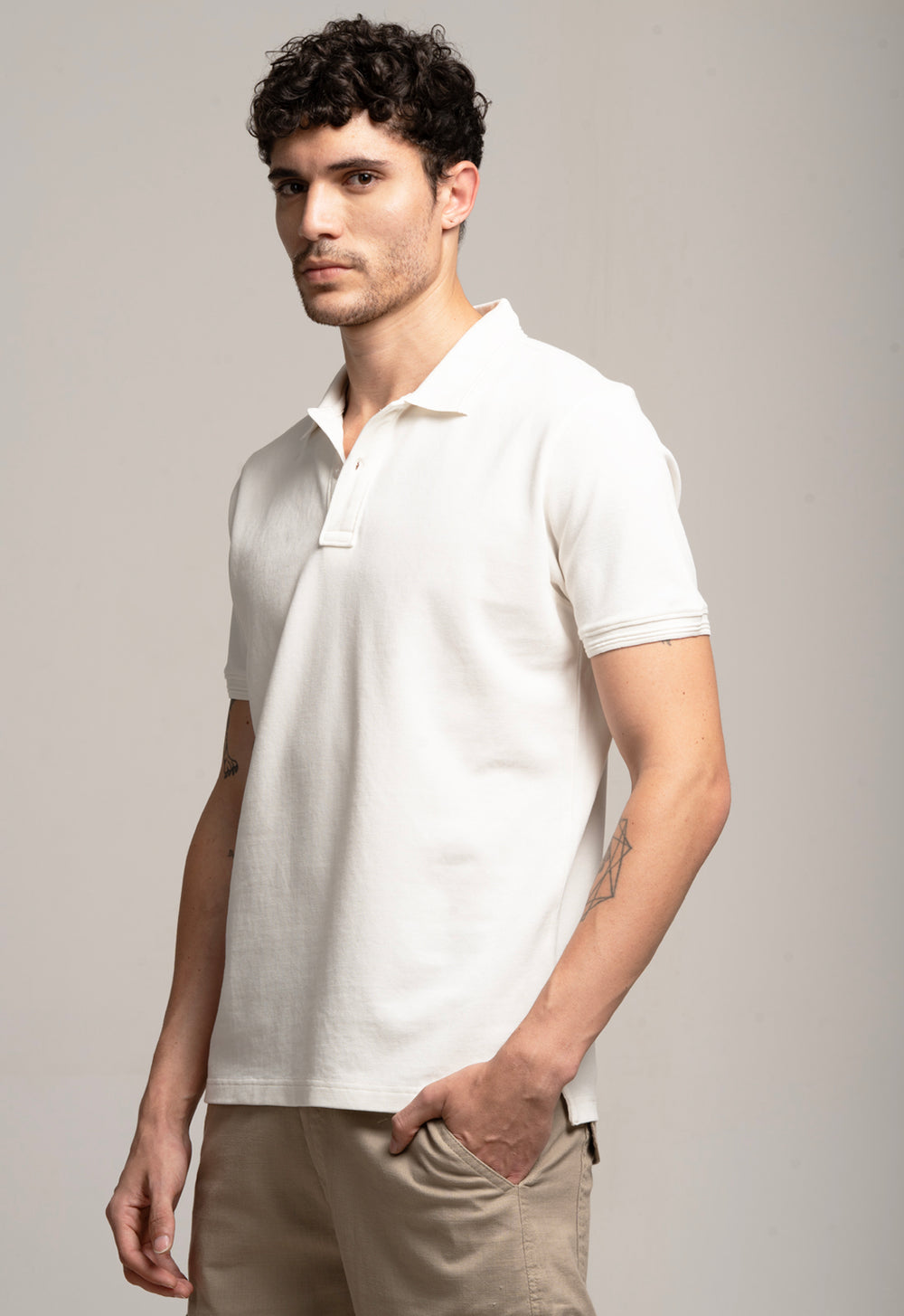 Man wearing a white polo shirt and beige pants against a gray background