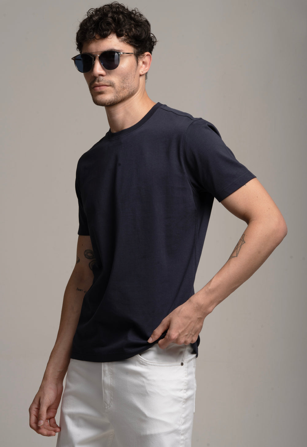 Man wearing a black t-shirt and white pants with sunglasses on a gray background