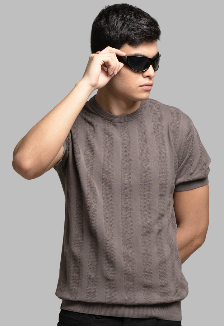 Man wearing a brown t-shirt and sunglasses against a plain background