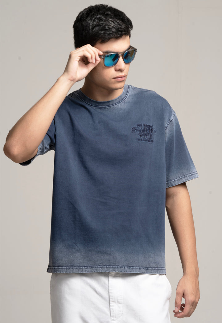 Person wearing a blue t-shirt with a logo, holding sunglasses, on a plain background