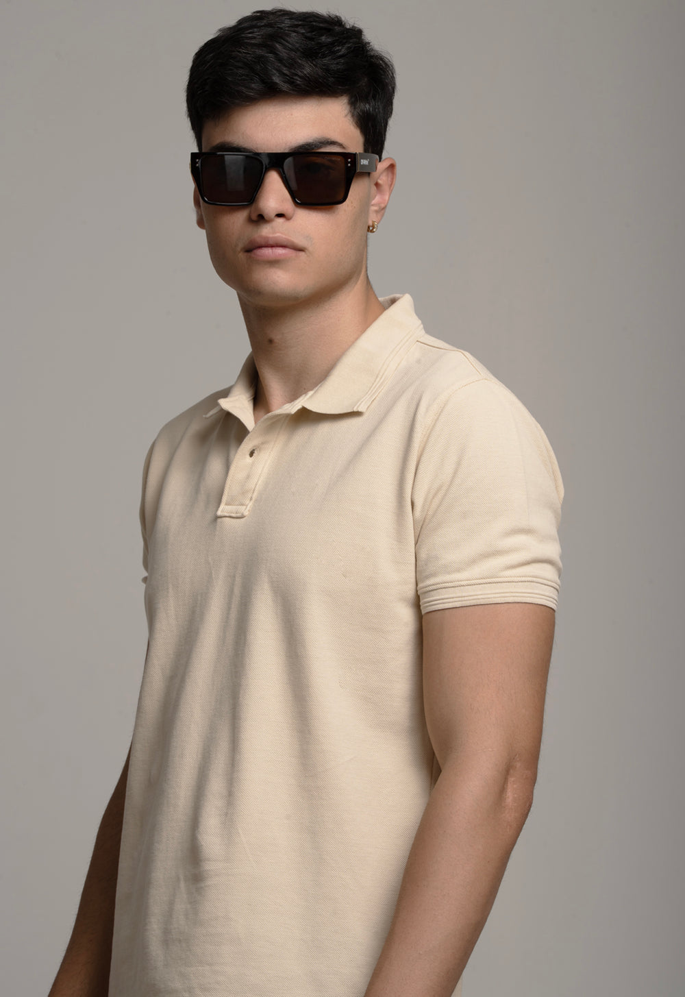 Man wearing a beige polo shirt and sunglasses against a gray background