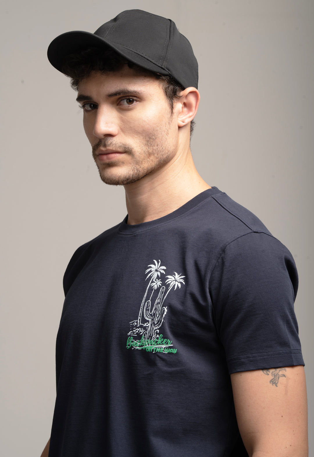 Man wearing a black t-shirt with a palm tree design and a cap on a gray background