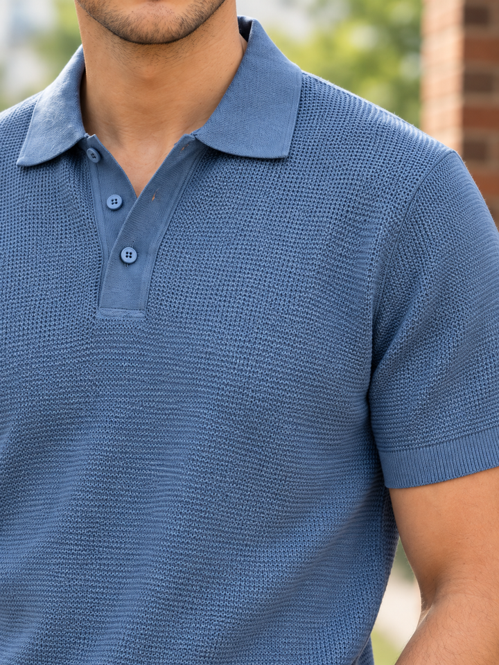 A close-up of a man wearing a textured blue short-sleeve polo shirt, showing the collar, three-button placket, and ribbed sleeve cuffs.