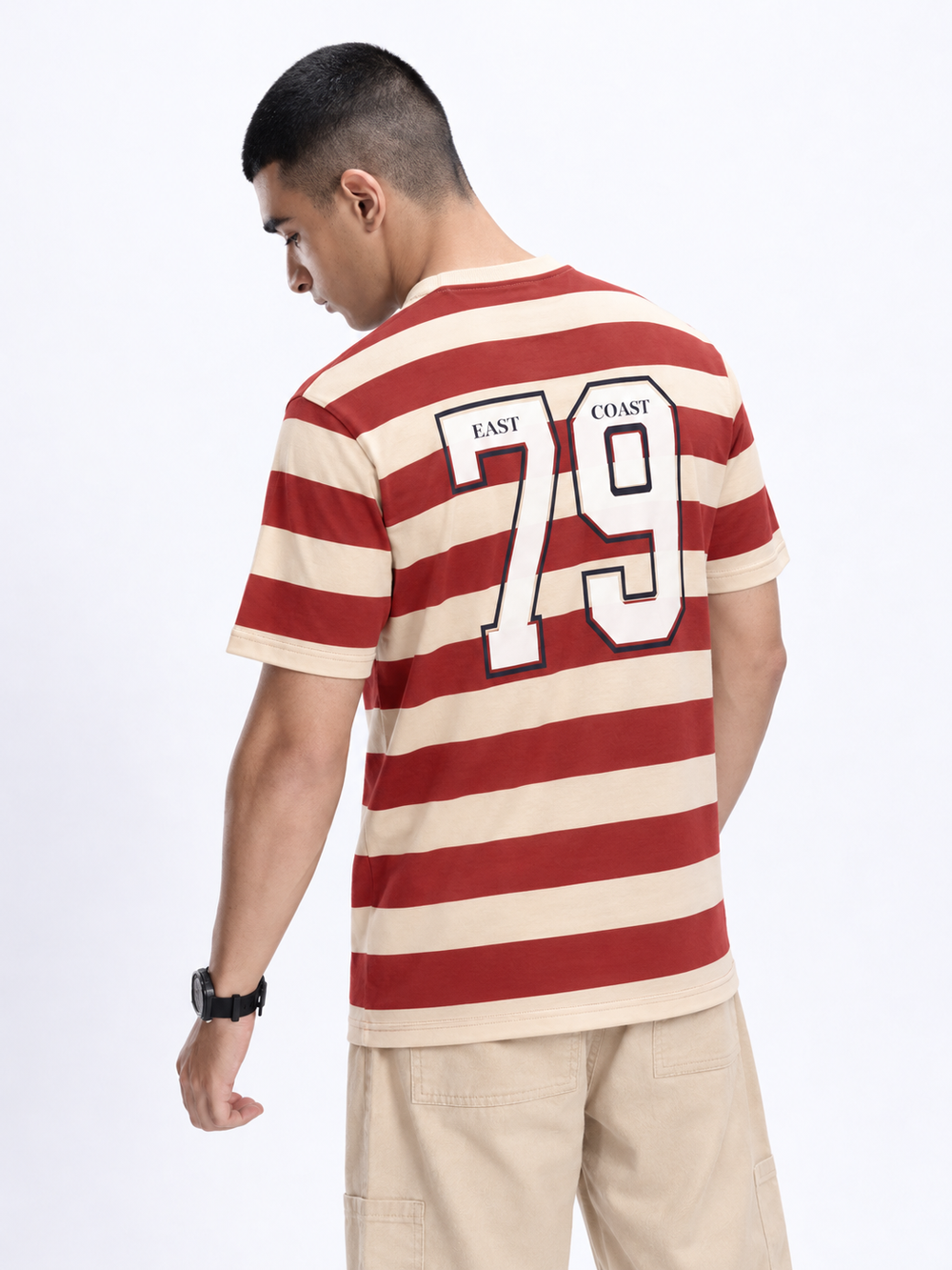 A man wearing a red and cream striped t-shirt with 'EAST COAST 79' printed on the back, shown from a three-quarters back view against a white studio background.