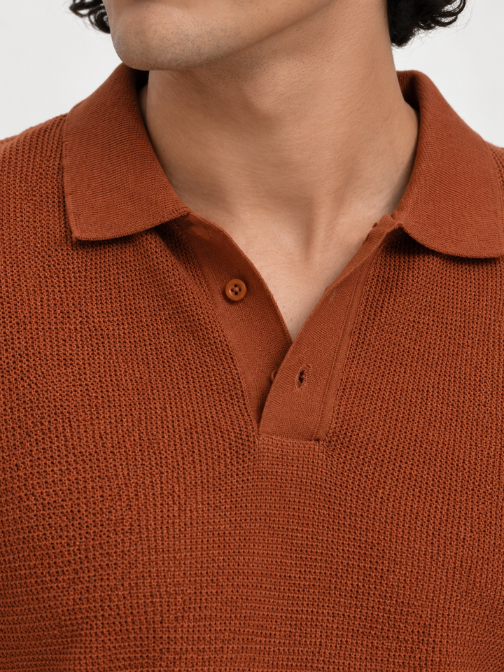 Close-up of a man wearing a textured rust-orange polo shirt, showing the collar, two-button placket, and knit fabric detail against a light neutral background.